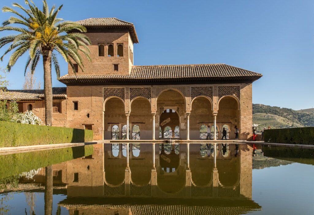 The stunning Alhambra arches and their reflection in the water create a picturesque scene under a clear blue sky.